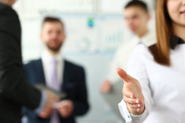 Dost canlısı genç şirket temsilcisi el sıkışmak için elini uzatıyor. Müşteriyi selamlamak ve iş arkadaşlarıyla poz vermek