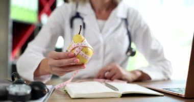 Doktor diyet için armut meyve ve vitaminli yiyecekler sunuyor. Beslenme uzmanı olgun sarı armudu ölçü bandıyla gösteriyor.