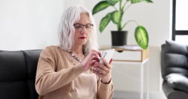 Evde cep telefonuyla konuşan ve oturma odasındaki kanepede dinlenen gülümseyen son sınıf öğrencisi kadın. Emekli kadın telefonda konuşuyor.