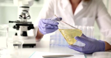Bilim adamı biyolog laboratuarda sarı yağ numunesiyle matarayı tutuyor. Kadın bilim adamı mikroskop altında araştırma için sıvı hazırlıyor.
