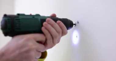 İnşaat işçisi matkapla beyaz duvara delik açıyor. Çalışma ve onarım için modern elektrikli araç
