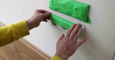 İnşaat işçisi, elektrikçi, duvarları boyamadan önce prizlere yeşil bant yapıştırıyor. Toprak ve tozdan prizleri kapat