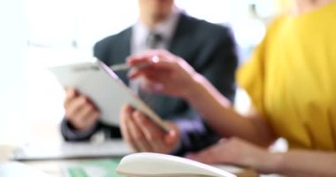 Adamın elinde ortak istatistiklerini gösteren tablet var. Kadın, masa ağır çekimde oturan elektronik cihazın kalemini ekrana doğrultuyor