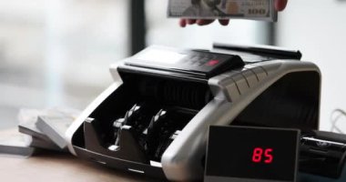 Adam ofis masasında duran banknotlara yığınla para koyuyor. Yönetici, toplam miktarı yavaş çekim tanımlamak için para sayma makinesinde s 'yi değiştirir