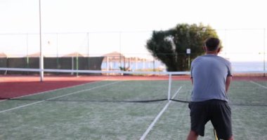 Sportif adam küçük sarı topa tenis raketiyle vuruyor. Erkek kişi tenis kortunda rakibiyle spor oyunu oynamaktan hoşlanır.