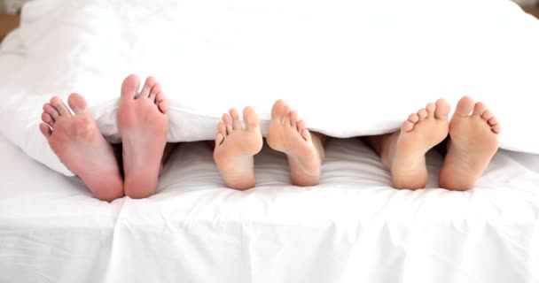 父母和小孩赤着脚在卧室里穿白毛毯移动 家人躺在床上伸出腿慢动作 — 图库视频影像