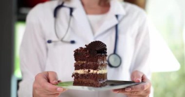 Kadın doktor elinde lezzetli çikolatalı pastayla tabağı tutuyor. Beyaz laboratuvar önlüklü kadın tatlı gösteriyor. Sağlıksız yeme konsepti