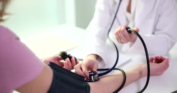 医師は女性の血圧を測定するために血友病計を使用しています カフラップ周りに上腕の女性患者座っているテーブルスローモーション — ストック動画