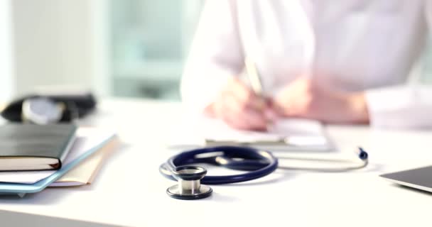 Stetoskop Doktorun Klinikteki Hastanın Tıbbi Geçmişini Yazmasına Karşı Beyaz Masada — Stok video