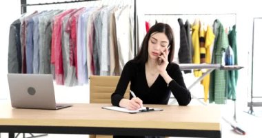 Özenli kadın telefonda müşteriyle konuşur. Detayları not alır. Esmer yönetici masada oturuyor ve kuru temizlemecide çalışıyor.