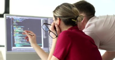 Bayan programcı, meslektaşına bilgisayar ekranında web sitesinin kodunu gösteriyor. Kadın ve erkek yavaş çekimde cihazın ekranına bakın