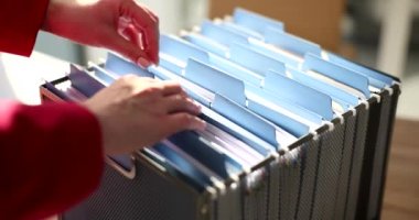 Sekreter analiz için muhasebe belgelerini içeren gerekli klasörü arıyor. Kadın ofis çekmecesindeki organize arşiv malzemelerini yavaş çekimde kontrol ediyor.