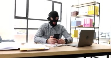 Kar maskeli dolandırıcı ve kulaklıklı 4K video bağlantısı ile cep telefonundan konuşuyor. İnternet dolandırıcılığı kavramı