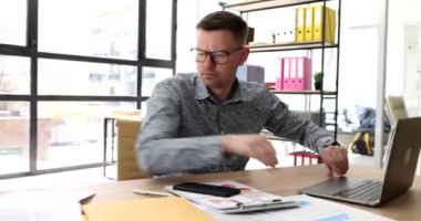 Ofis 4K filminde gözlüklü bir işadamı masaüstünde belge arıyor. İş konseptinde kağıtlar