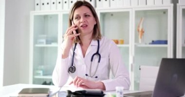 Mutlu doktor masada oturup hastayla telefonda konuşuyor. Uzaktan tıbbi yardım ve danışma