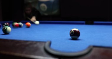 Mavi kumaş üzerinde bilardo oyunu. Bilardo masasında numara yazan bilardo topları topa vuruyor.