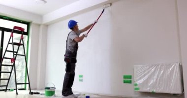 İnşaatçı duvarı uzun silindirle boyuyor. Tamir ve dekorasyon kavramı