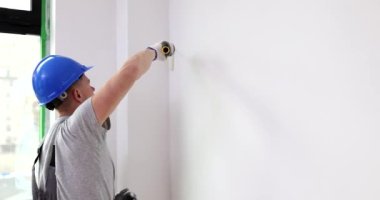 Sert şapkalı bir ressam daire duvarını tekerlekli fırçayla boyuyor. Boyama ve ev tamiri.