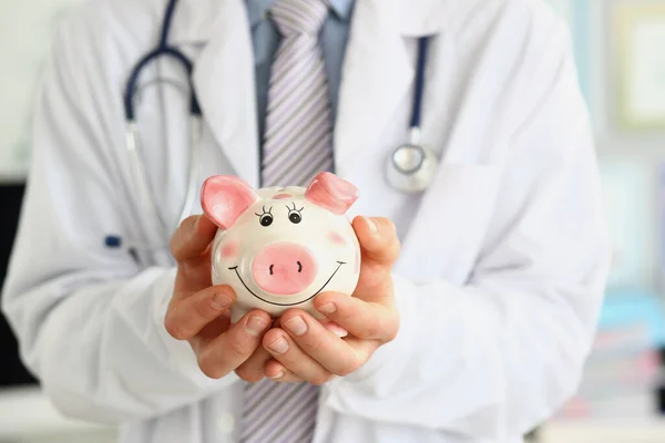 身穿白衣的医生手牵着快乐微笑的小猪银行 医疗经济保健储蓄和保险概念 — 图库照片