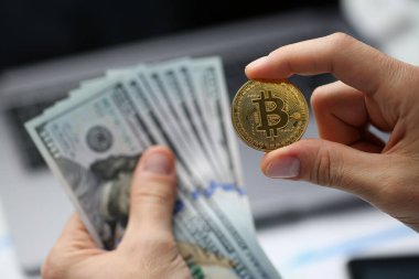 İnsan eli 100 dolarlık banknotları ve altın bitcoin paraları tutar. Kripto para birimi geliri ve mali yatırımları