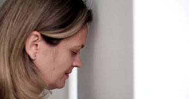 Hüsrana uğramış bir iş kadını, beyaz duvara yaslanmış, yakın plan. Zihinsel ve fiziksel acı, yavaş çekim