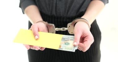 Elleri kelepçeli bir kadın bir zarftan dolar çıkarır, elleri yakın çekimde. Rüşvet, yasadışı para