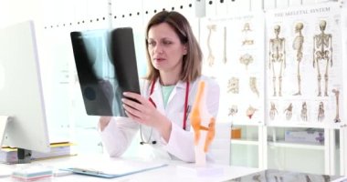 Klinikte oturan doktor dizinin röntgenine bakıyor, yakından. Ortopedist muayenesi, ayak yaralanması.