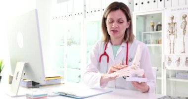 Kadın bir cerrah, ayağın anatomik modelini tutuyor. Yakın plan. Bir nörologun muayenesi, zaman ayarlı.
