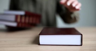 Kadın eli masaya bir yığın kırmızı kitap serer, yakın plan. Ansiklopedik bilgi, eğitim