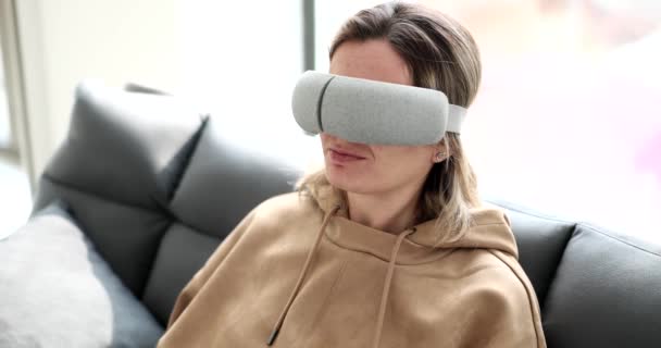 一个年轻的女人坐在沙发上 带着一个虚拟的睡眠面具 一个特写镜头 一个增加的外观 放松装置 — 图库视频影像