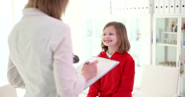 陽気な女の子は医者を見て クローズアップ 医者は子供の症状を学ぶでしょう — ストック動画
