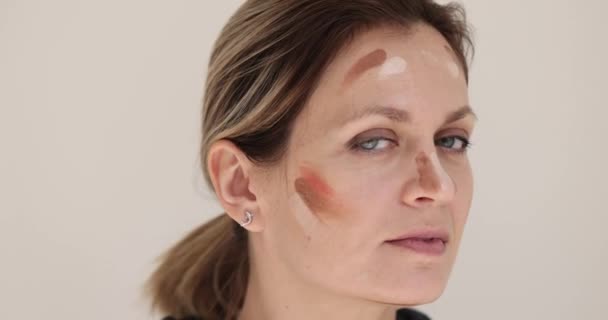 彼女の顔に化粧品を持つ若い女性 クローズアップ メイクトレーニング クリームの選択 スローモーション — ストック動画
