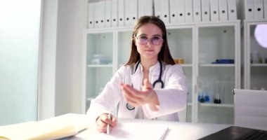 Genç doktor masada oturur elini ileri uzatır, yakın plan. Klinikte dostça karşılama.