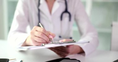 Masada oturan doktor beyaz bir klasöre yakın çekim yazıyor. Terapiste bir ziyaret, hasta kartı.