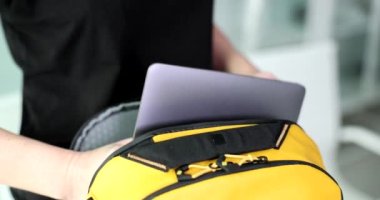 Genç kadın elleri, sarı bir sırt çantasına dizüstü bilgisayar koymuş. Yakın plan. Suç ortağı, hafif seyahat eden, yavaş çekim