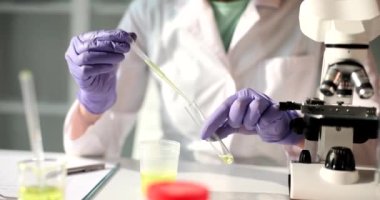 Laboratuvar asistanı bir pipetle birlikte bir mataraya sarı bir sıvı döküyor, yakın plan. Laboratuvar testleri, tanı testleri