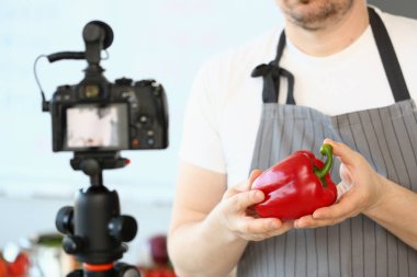 Gıda blogcusu sağlıklı beslenme ve diyet içeriği yaratıyor. Erkek aşçı elinde kırmızı tutar ve kameraya video çeker.