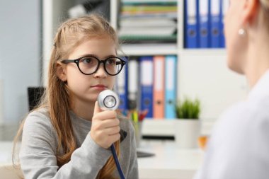Tıbbi muayenedeki kız çocuğunda stetoskop var. Gülümseyen çocuk doktor pediatriste güveniyor