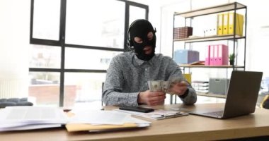 Kulaklıklı, mikrofonlu, kar maskeli bir internet operatörü bilgisayar masasında para sayıyor. Siber suçlar ve mali suçlar İnternet 'te