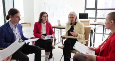 Profesyonel eğitmen yaşlı kadın eğitimciler ofiste odaklanmış yöneticiler yetiştiriyor. Konsantre olmuş genç meslektaşlar kıdemli konuşmacıları dinliyor ve beyin fırtınası üzerine proje fikirleri sunuyorlar