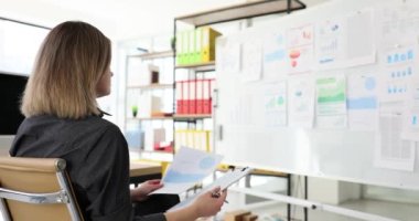 Beyaz yönetim kurulundaki istatistiksel bilgileri kullanarak evrak işleri yapan hevesli bir bayan yönetici. Kağıt raporunda verileri inceleyen pazarlama analisti