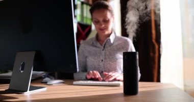 Oturma yerindeki modern hava nemlendirici aygıtı. İnternet üzerinde bilgisayar kullanan serbest çalışan kadın ofis odasındaki gerekli yağ dağıtıcıdan aromaterapi buharının tadını çıkarıyor.