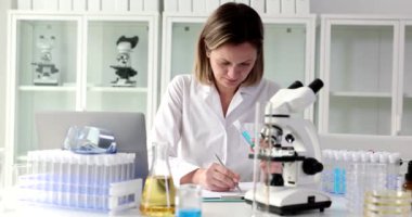 Bilim adamı biyolog mavi sıvıyla test tüpünü tutuyor ve not alıyor. Kimya laboratuarı asistanı araştırma laboratuvarında bilimsel deneyler yürütüyor.