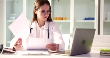 Odaklanmış tıp doktoru öğrenci kağıt belgelere bakıyor ve sağlık sigortası sözleşmelerini okuyor. Kadın doktor klinikteki hastalıkların tedavi geçmişine veya raporlarına bakıyor.