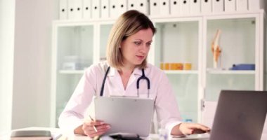 Kadın doktor tıbbi belgeleri inceler ve dizüstü bilgisayara bakar. Tıbbi bakım ve yardım
