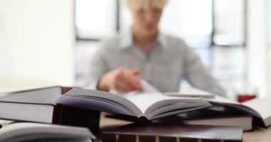 Kitaplarla dolu bir masada oturan bayan öğrenci ya da ofis yöneticisi manzarası. Stajyer ödevleri hazırlarken ya da sınavlara hazırlanırken eğleniyor