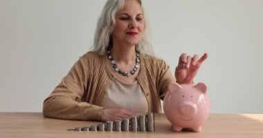 Mutlu orta yaşlı kadın domuz kumbarasına para koyar ve gelecek için para biriktirir. Yatırım ve aile tasarrufu yapan emekli bir kadın.