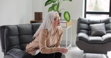 Sırt ağrısı çeken yaşlı bir kadın kanepeden kalkar. Yaşlılarda sırt ağrısı teşhis ve tedaviye neden olur