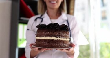 Doktor, klinikte çok lezzetli kalorili çikolatalı pasta tutuyor. Beslenme uzmanı sağlıksız yiyecek örneği gösteriyor.