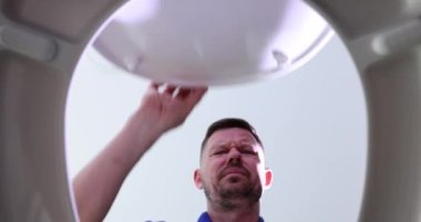 Muslukçu adam tuvalet kapağını açıyor ve cep telefonunun 4K filmini çıkarıyor. Telefon kavramının dikkatsiz kullanımı